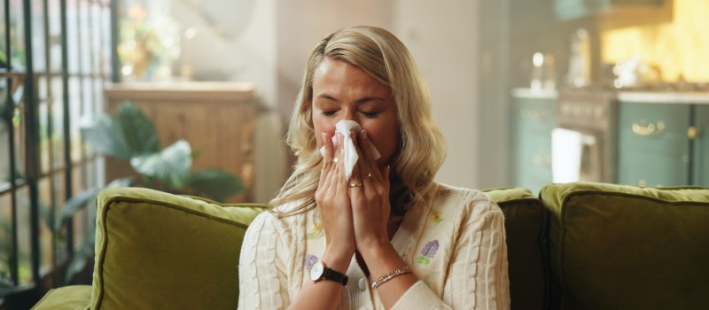 Woman sneezing on couch indoors