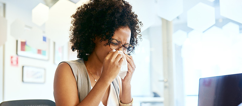 Woman sneezing at office desk